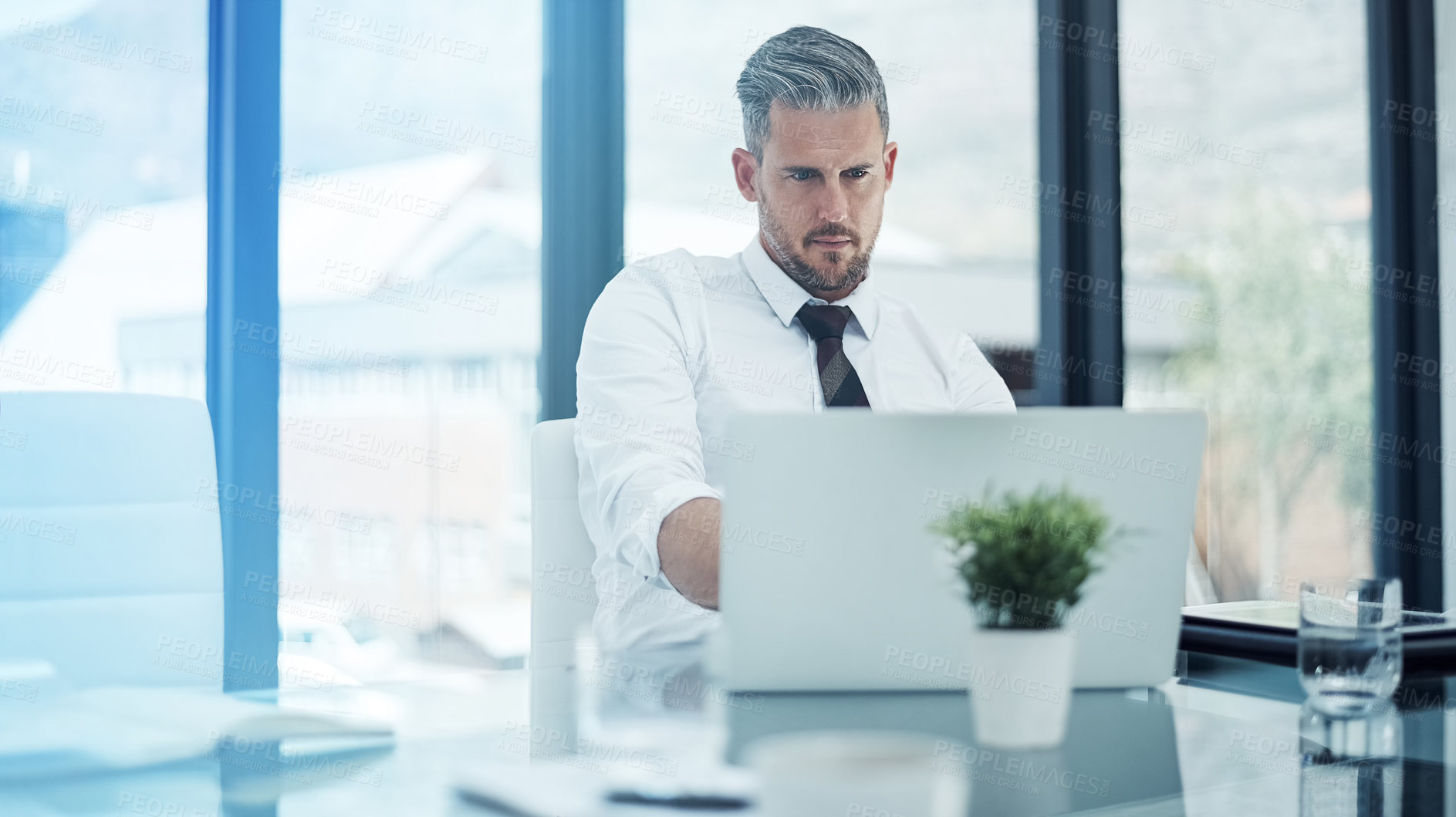 Buy stock photo Shot of a corporate businessman working on a laptop in an office