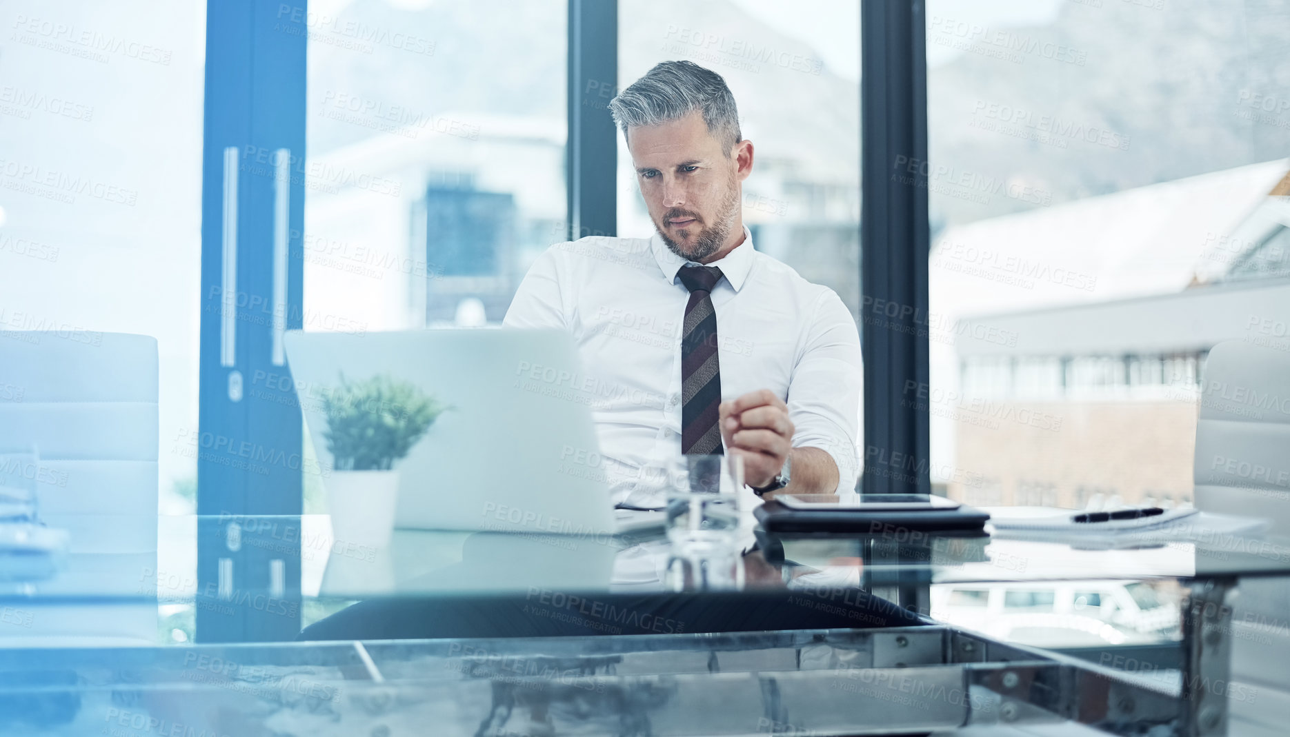 Buy stock photo Shot of a corporate businessman working on a laptop in an office