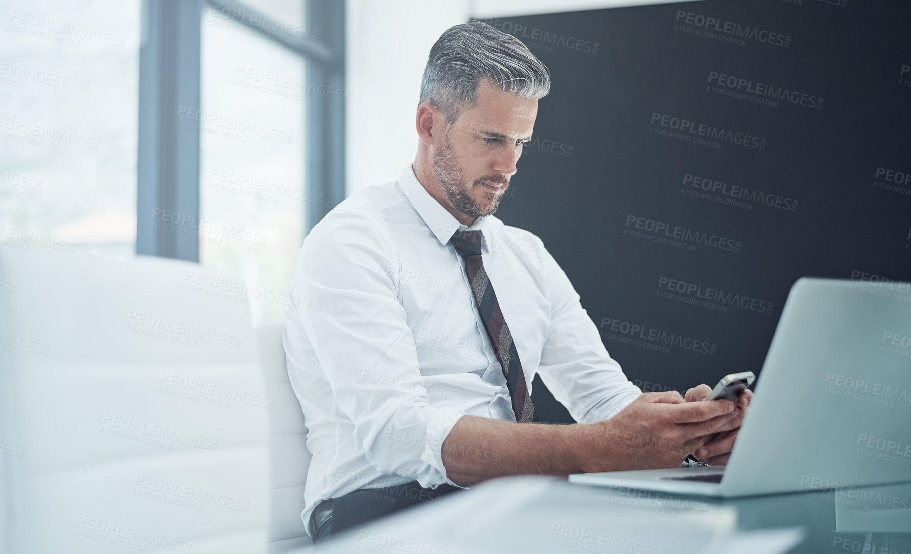 Buy stock photo Shot of a corporate businessman texting on a cellphone while working in an office