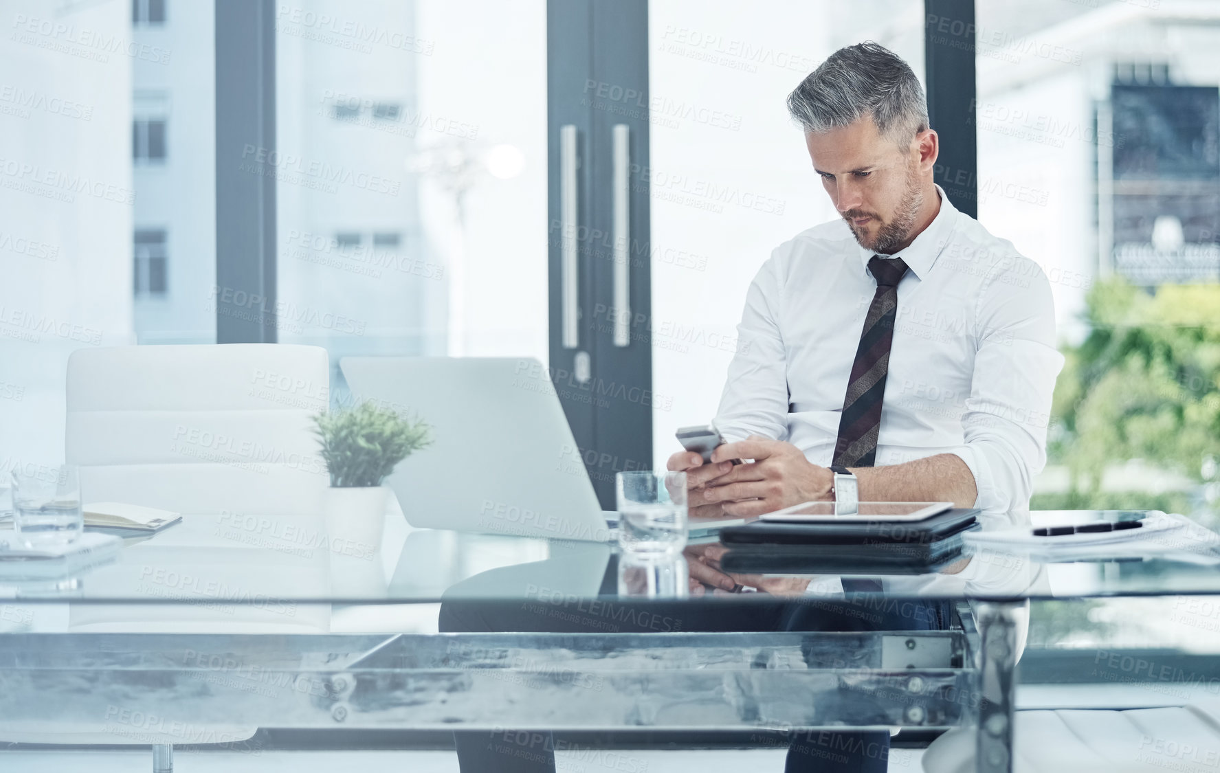 Buy stock photo Shot of a corporate businessman texting on a cellphone while working in an office