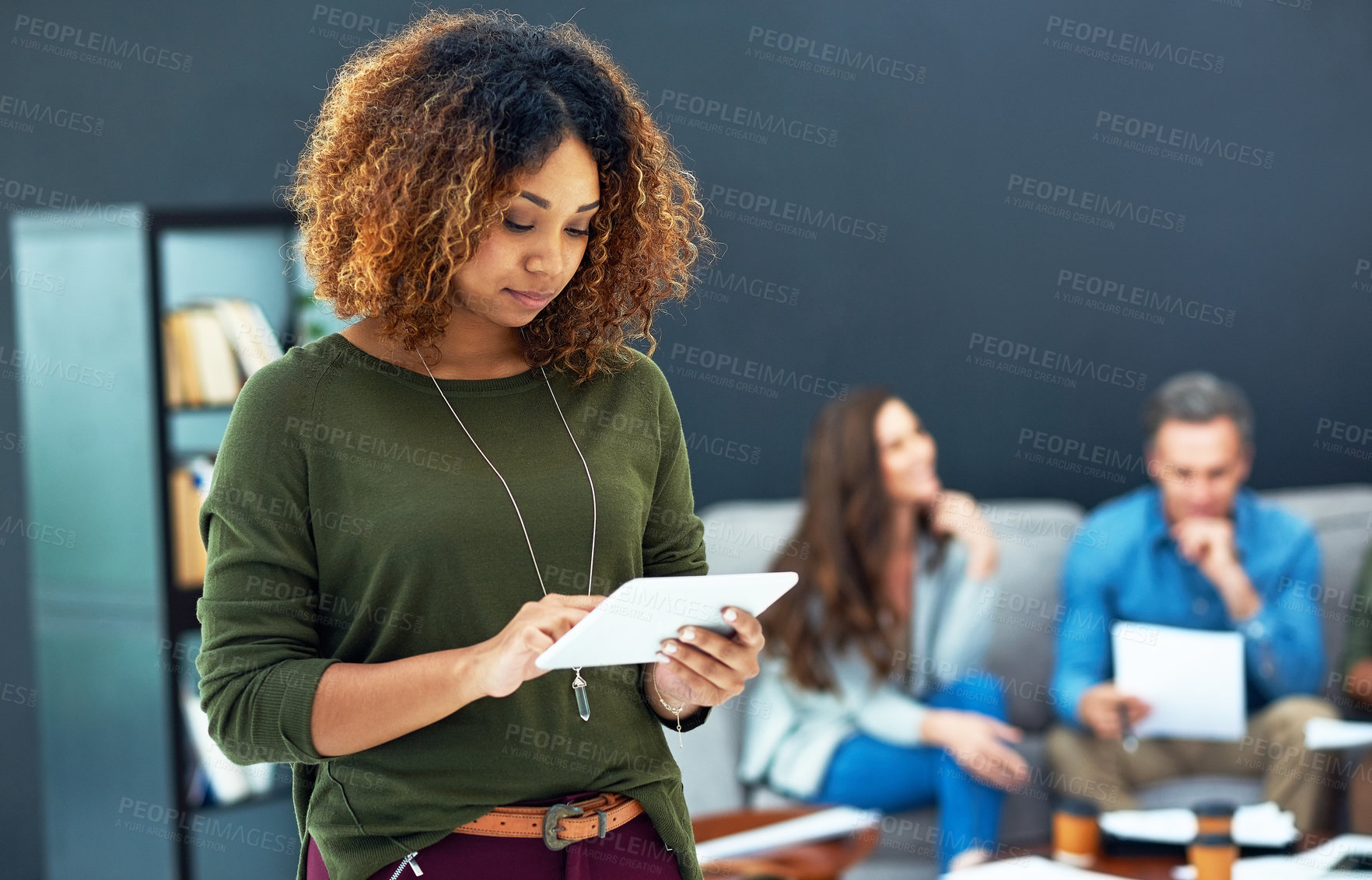 Buy stock photo Shot of a young businesswoman using a digital tablet with her team in the background