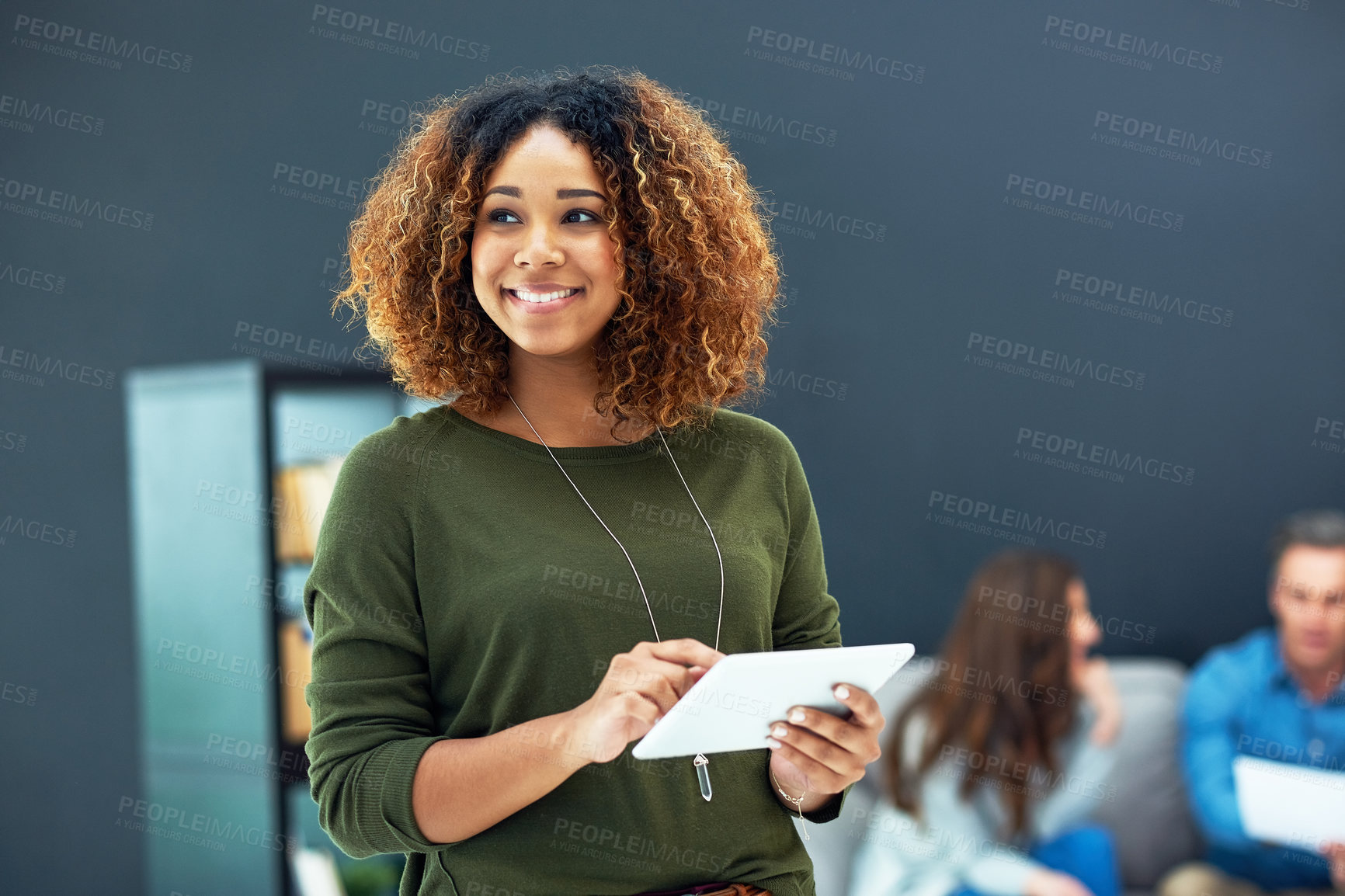 Buy stock photo Shot of a young businesswoman using a digital tablet with her team in the background