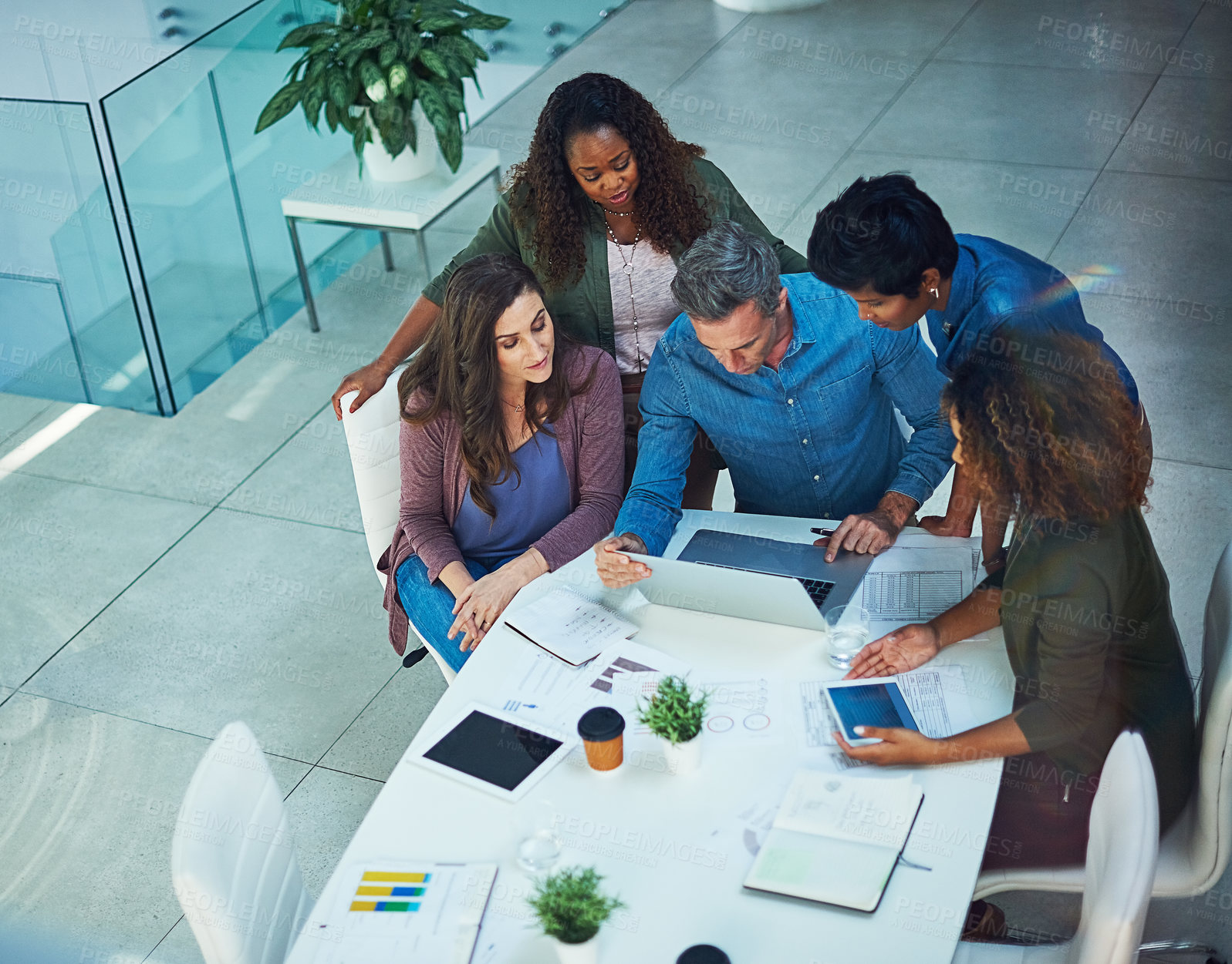 Buy stock photo Shot of a group of designers gathering around a man using a laptop in a meeting