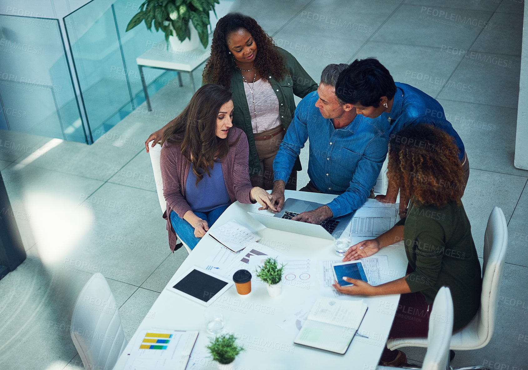 Buy stock photo Shot of a group of designers gathering around a man using a laptop in a meeting