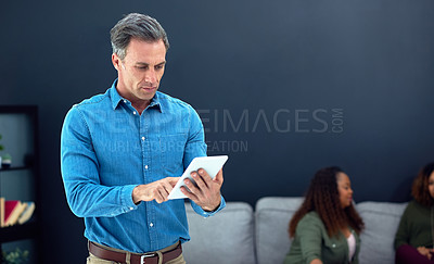 Buy stock photo Shot of a mature businessman using a digital tablet with his team in the background