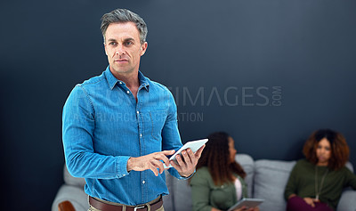 Buy stock photo Shot of a mature businessman using a digital tablet with his team in the background