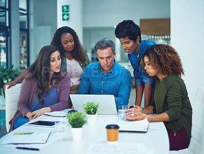 Buy stock photo Shot of a group of designers gathering around a man using a laptop in a meeting