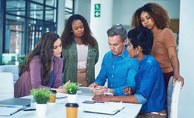 Buy stock photo Shot of a group of designers gathering around a man using a tablet in a meeting