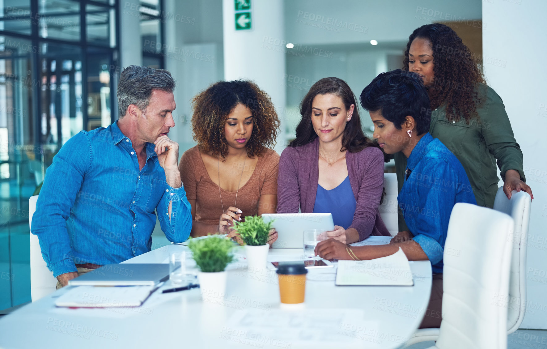 Buy stock photo Shot of a group of designers gathering around a woman using a tablet in a meeting