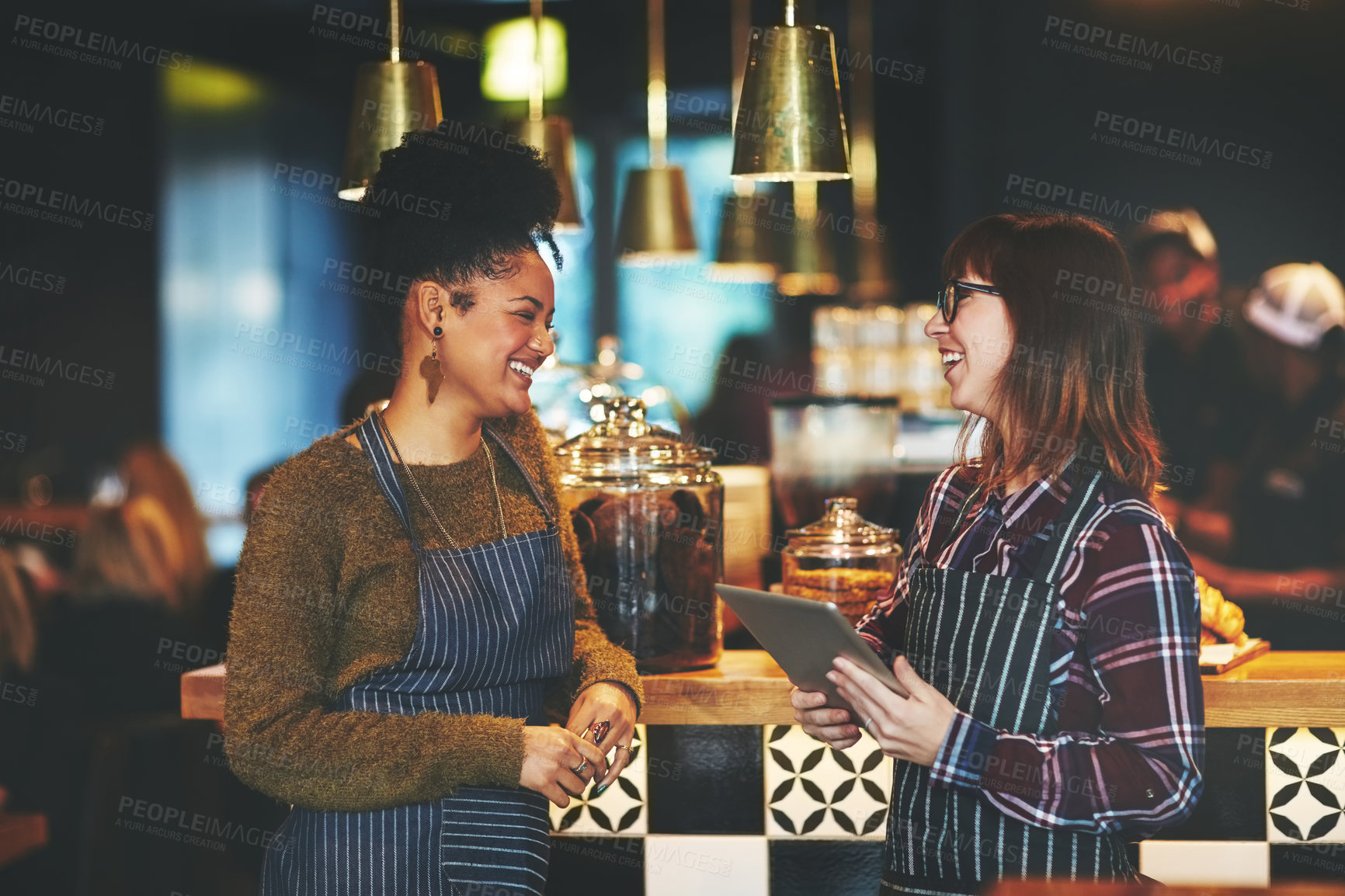 Buy stock photo Shot of two young women using a digital tablet together while working at a coffee shop