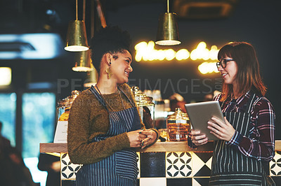 Buy stock photo Shot of two young women using a digital tablet together while working at a coffee shop