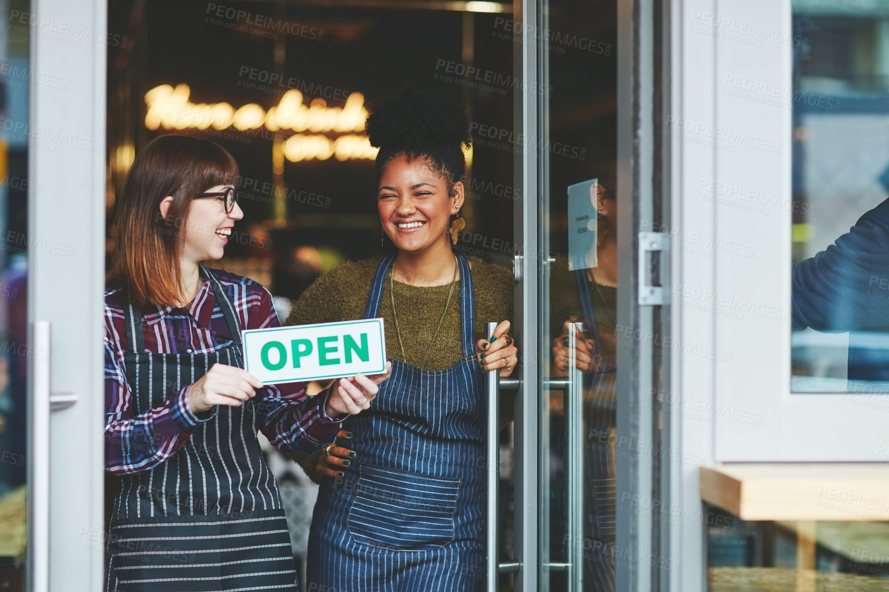 Buy stock photo Shot of two young women holding up an open sign in their coffee shop