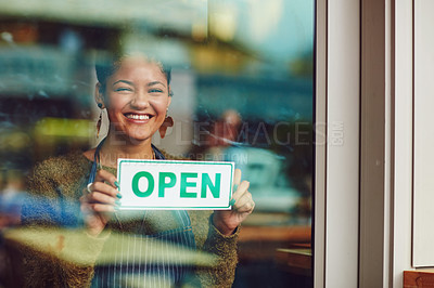 Buy stock photo Shot of a young woman holding up an open sign in her coffee shop