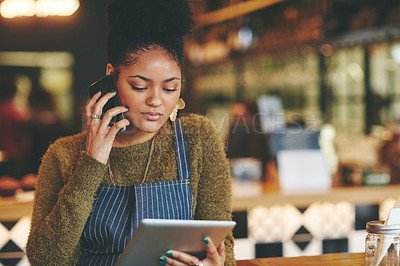 Buy stock photo Shot of a young woman using a phone and digital tablet while working at a coffee shop