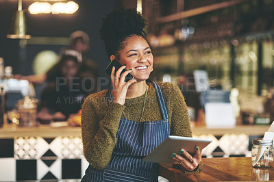 Buy stock photo Shot of a young woman using a phone and digital tablet while working at a coffee shop