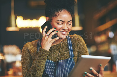 Buy stock photo Shot of a young woman using a phone and digital tablet while working at a coffee shop