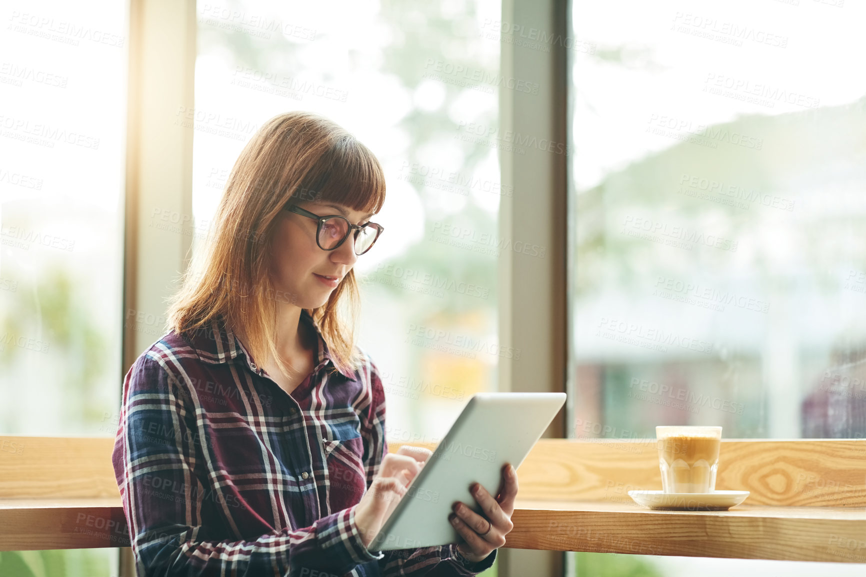 Buy stock photo Shot of a young woman using a digital tablet at a coffee shop