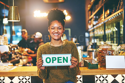 Buy stock photo Shot of a young woman holding up an open sign in her coffee shop