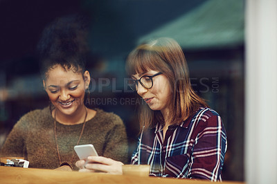 Buy stock photo Cropped shot of two young friends looking at something on a cellphone in a cafe