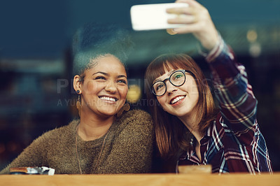 Buy stock photo Cropped shot of two young friends taking a selfie together in a cafe