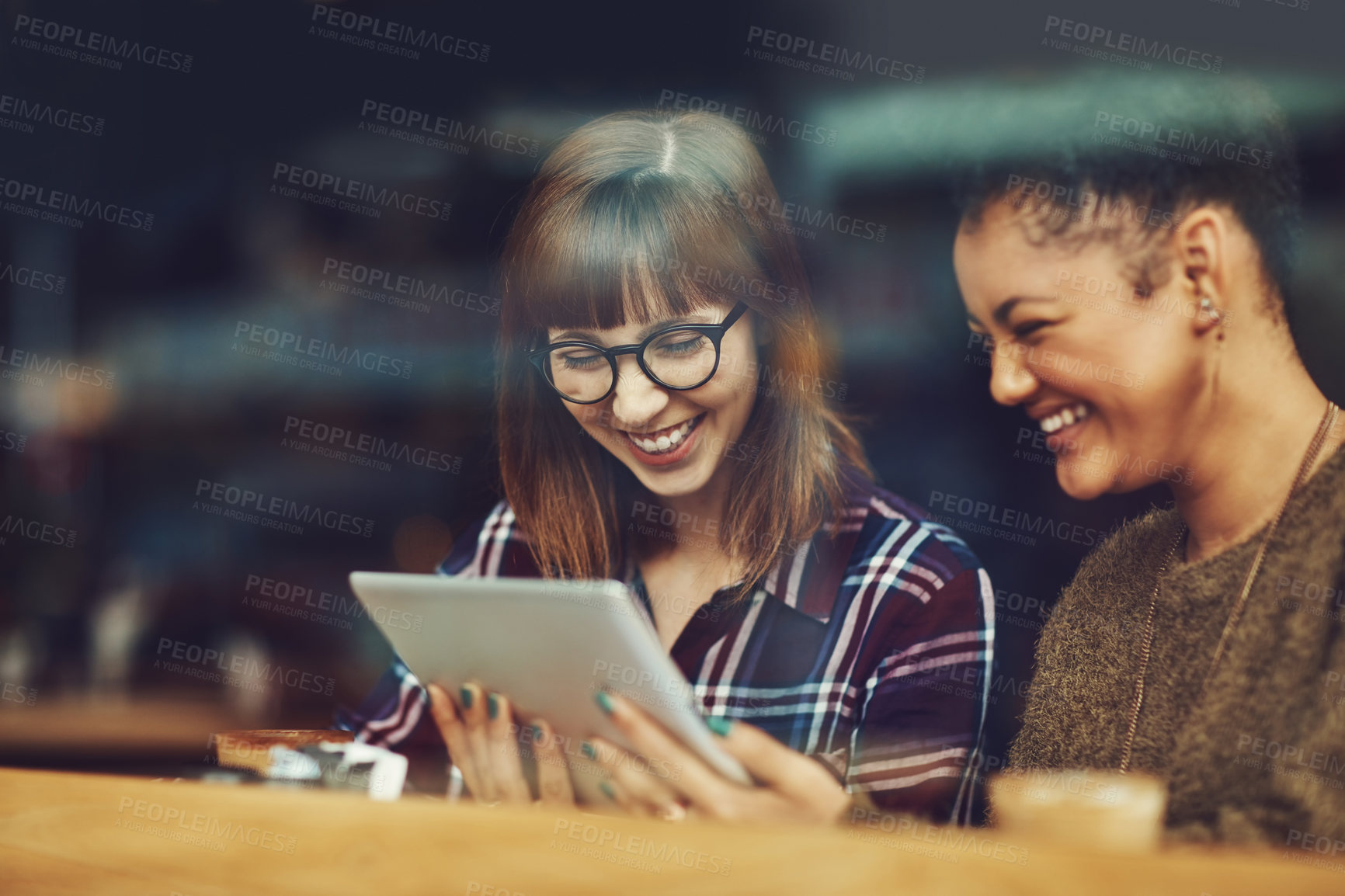 Buy stock photo Cropped shot of two young friends looking at something on a digital tablet in a cafe