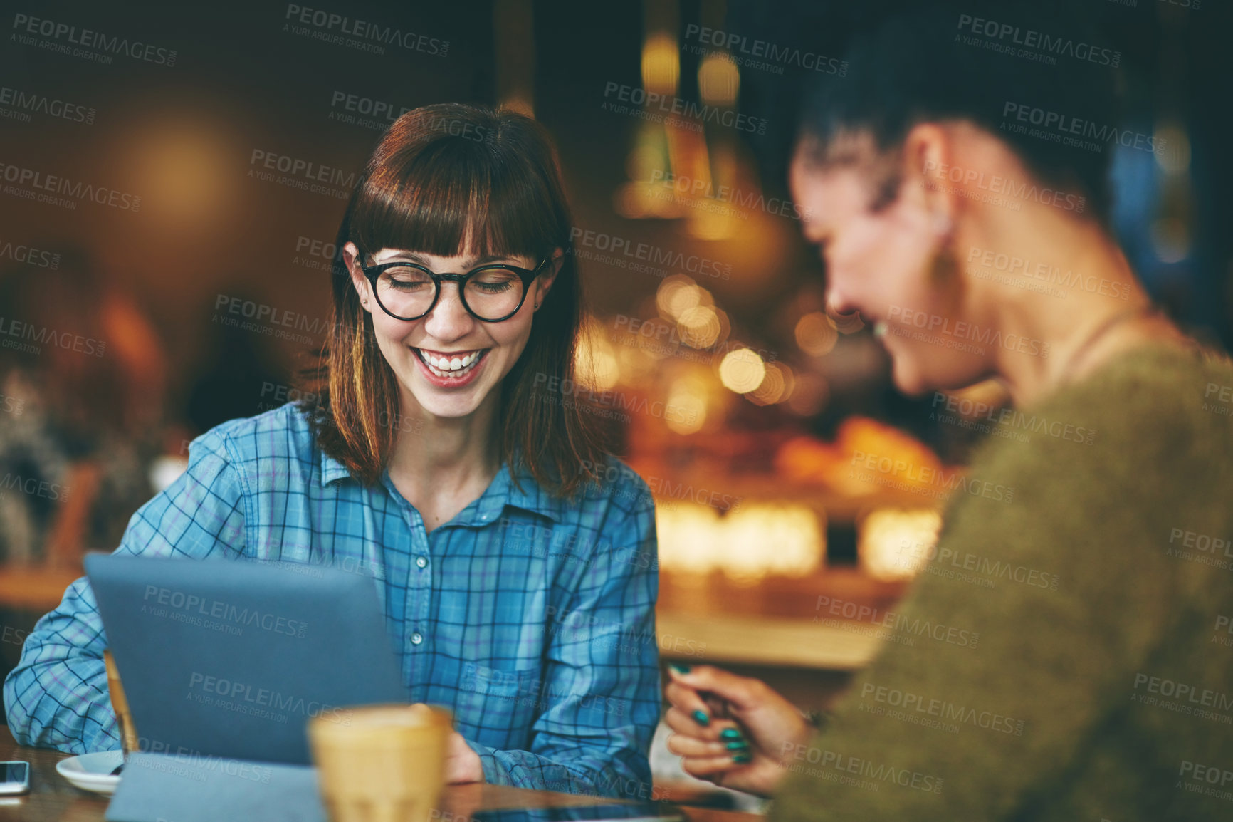 Buy stock photo Shot of two young friends looking at something on a digital tablet in a cafe