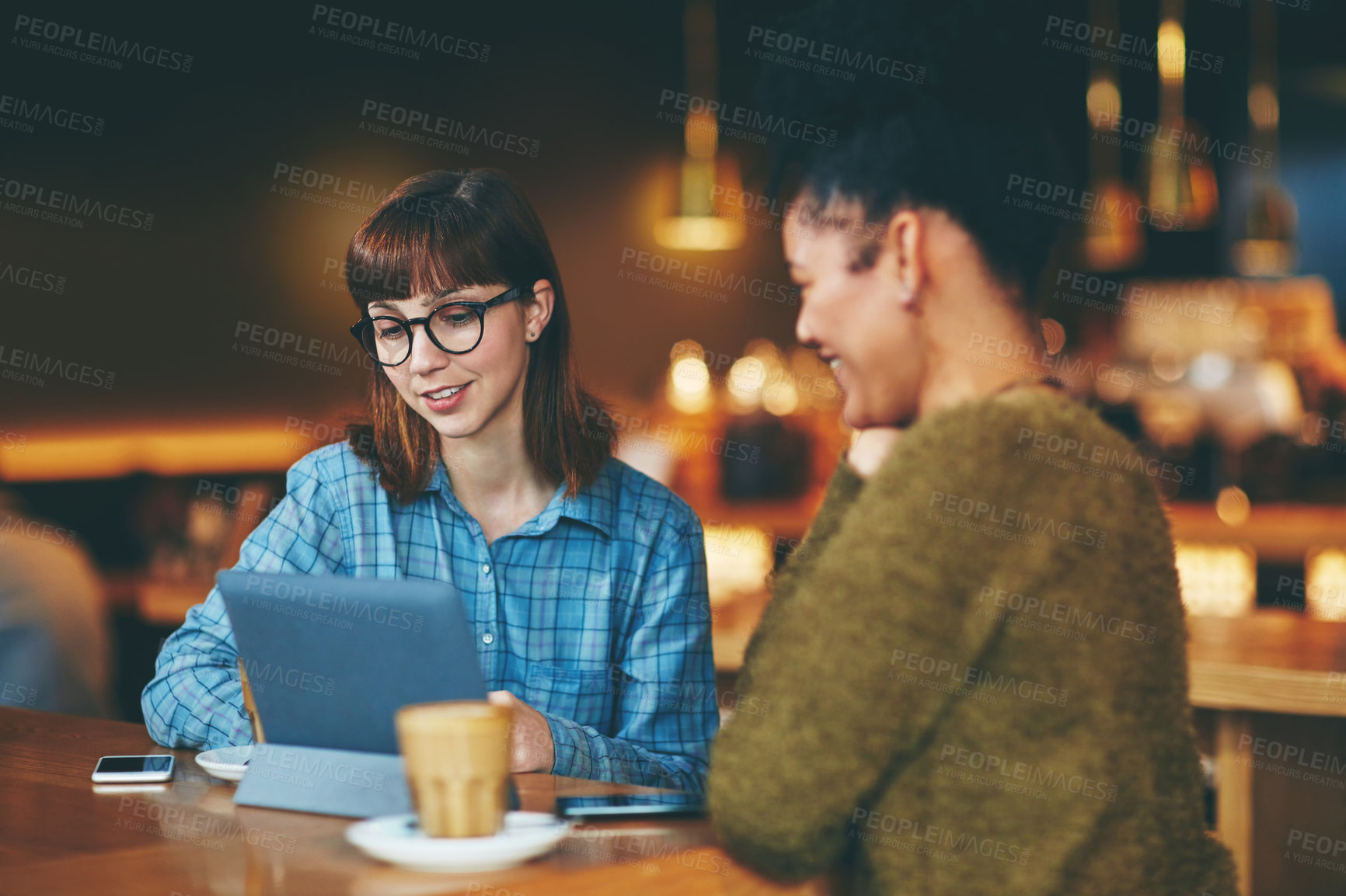 Buy stock photo Shot of two young friends looking at something on a digital tablet in a cafe