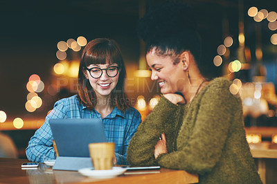 Buy stock photo Shot of two young friends looking at something on a digital tablet in a cafe