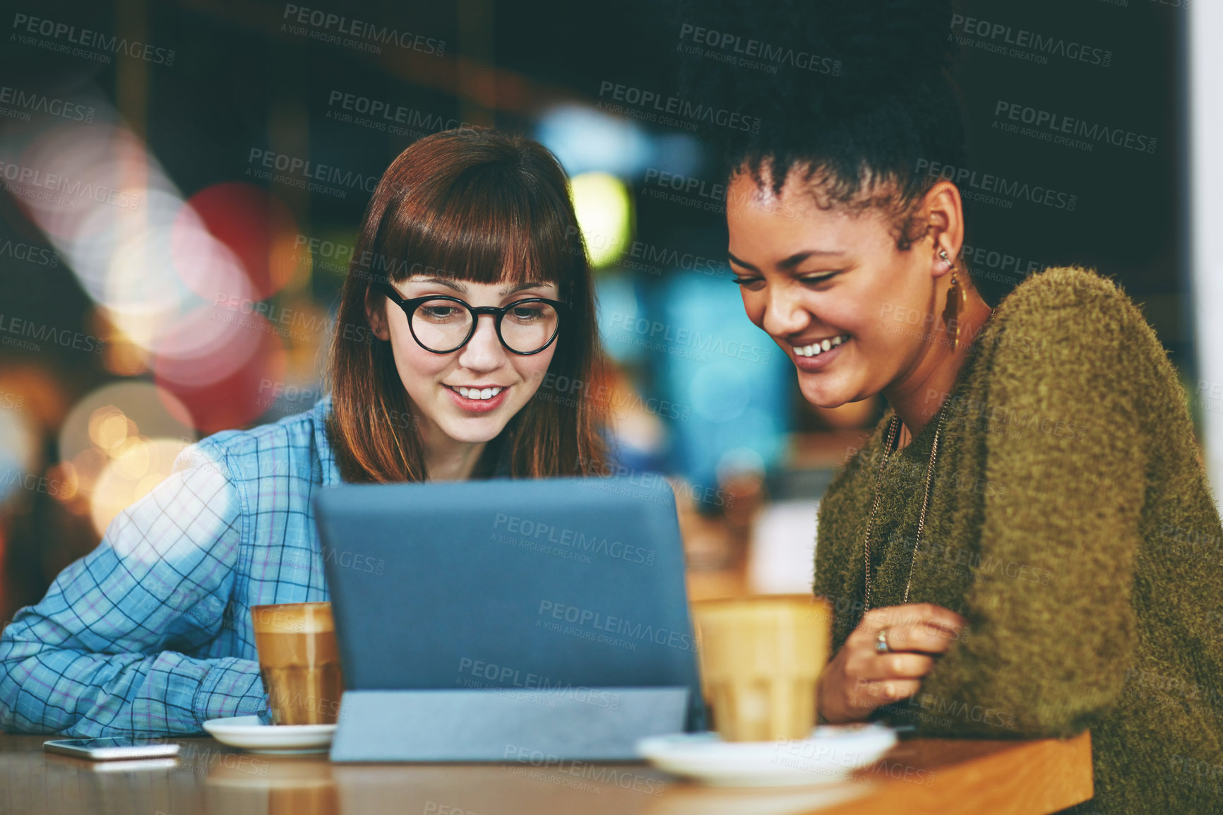 Buy stock photo Shot of two young friends looking at something on a digital tablet in a cafe