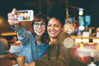 Buy stock photo Shot of two young friends taking a selfie together in a cafe