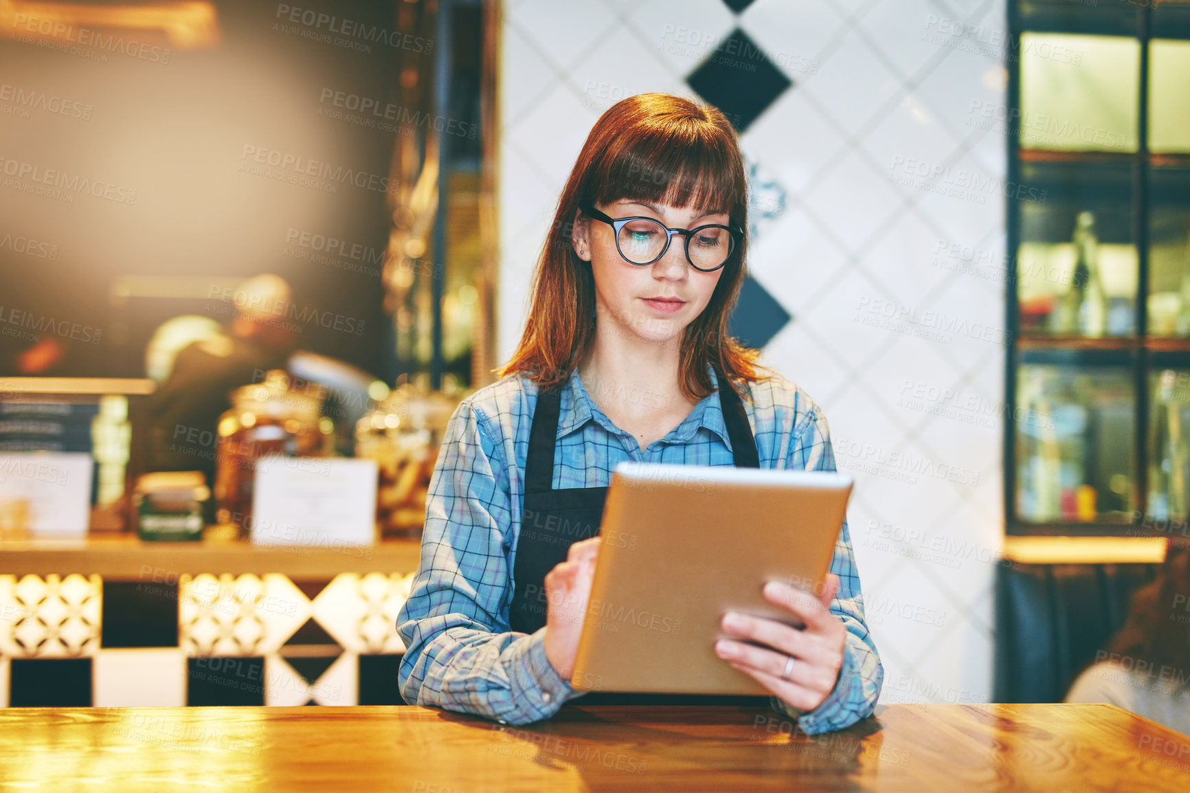 Buy stock photo Shot of a young business owner using a digital tablet in her cafe