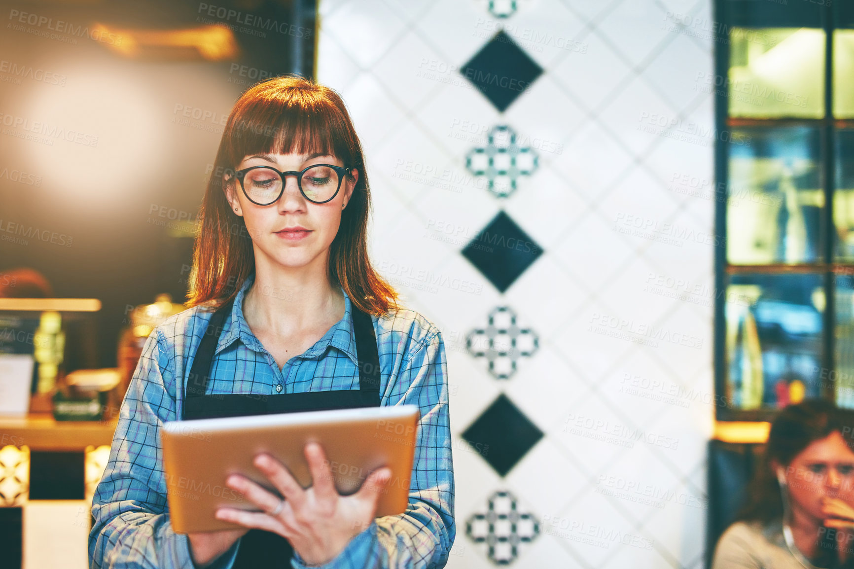 Buy stock photo Shot of a young business owner using a digital tablet in her cafe