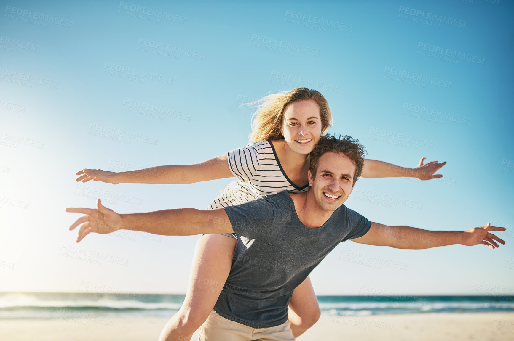 Buy stock photo Shot of a happy young couple enjoying a piggyback ride at the beach