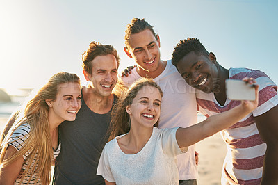 Buy stock photo Shot of a happy group of friends taking selfies together at the beach