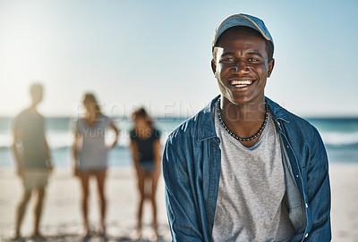 Buy stock photo Portrait of a happy young man posing on the beach with his friends in the background