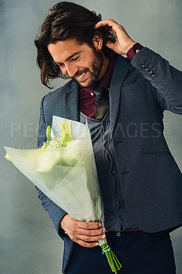 Buy stock photo Studio shot of a stylishly dressed handsome young man smiling and holding a bouquet of flowers