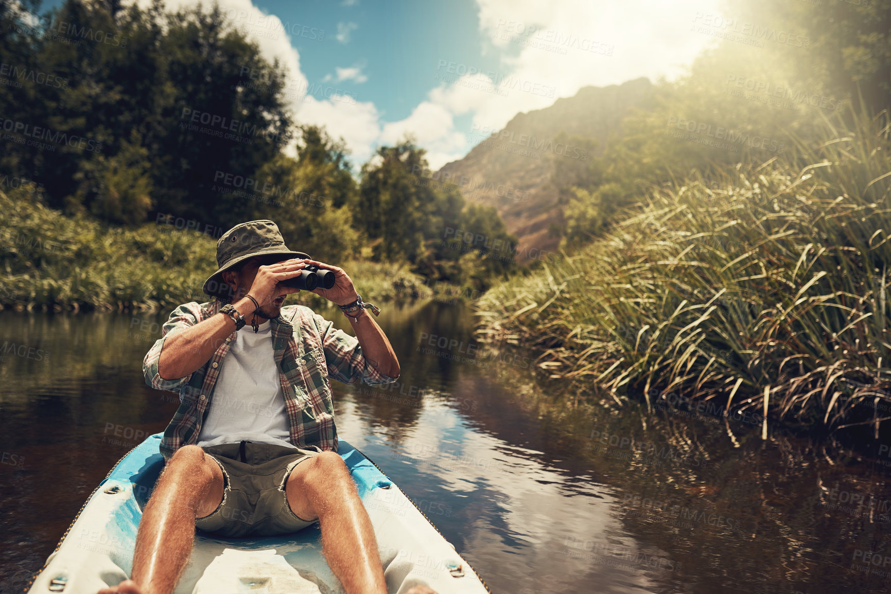 Buy stock photo Cropped shot of a young man looking through his binoculars while enjoying a canoe ride on the lake