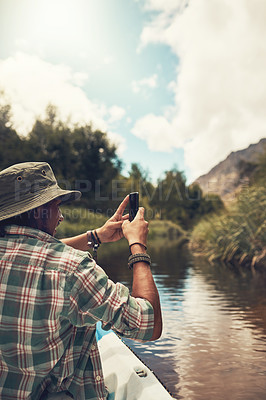 Buy stock photo Rearview shot of a young man taking photos on his cellphone while enjoying a canoe ride on the lake