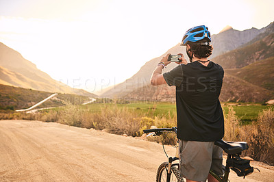 Buy stock photo Cropped shot of a young man taking a photo while cycling along a trail