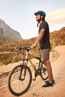 Buy stock photo Shot of a young man looking thoughtful while standing with his bike on a trail