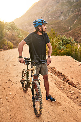 Buy stock photo Shot of a young man looking thoughtful while standing with his bike on a trail
