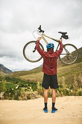 Buy stock photo Rearview shot of a young man standing with his bike raised in victory outside