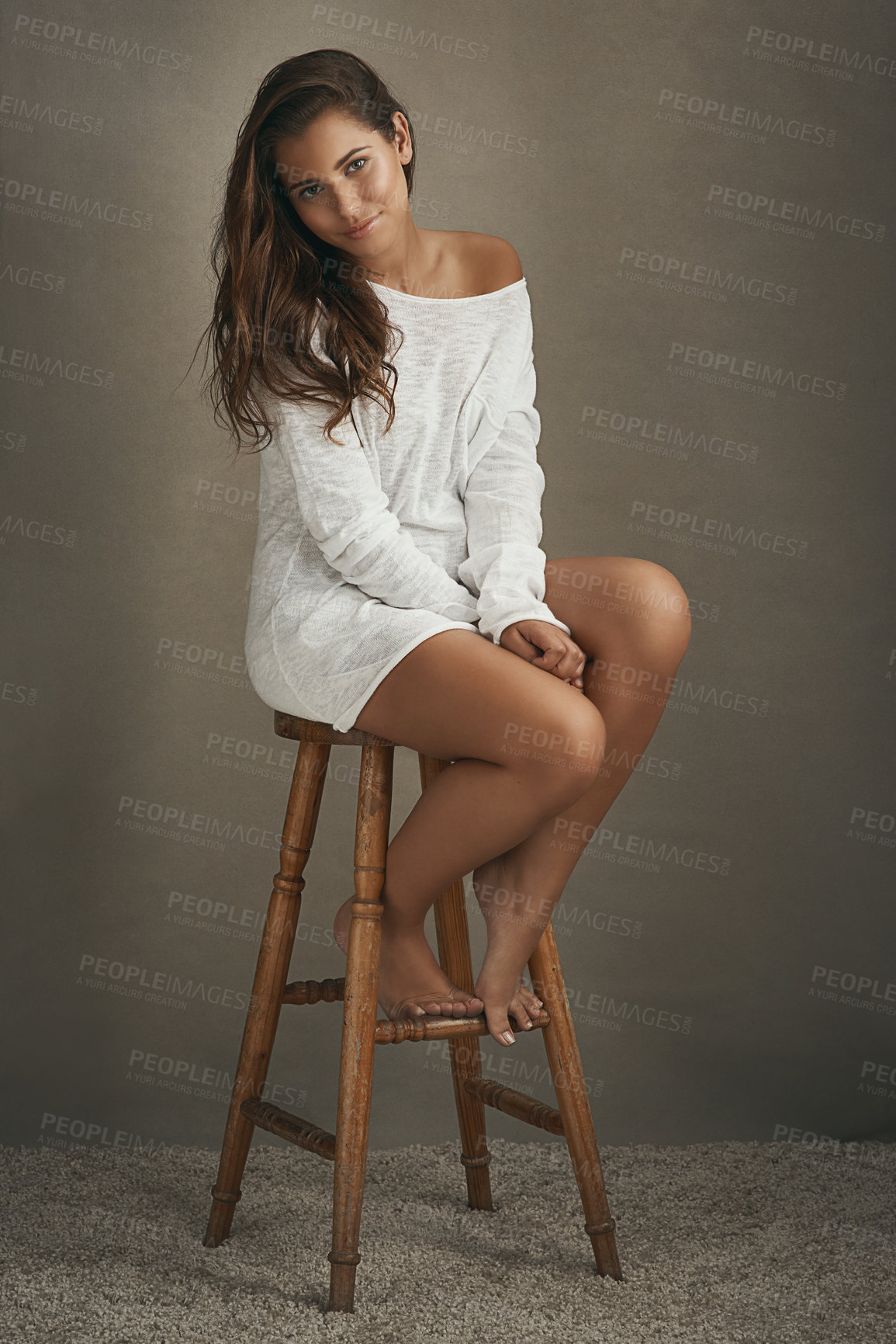 Buy stock photo Portrait of a beautiful young woman sitting on a stool against a brown background in studio