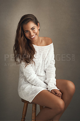 Buy stock photo Portrait of a beautiful young woman sitting on a stool against a brown background in studio