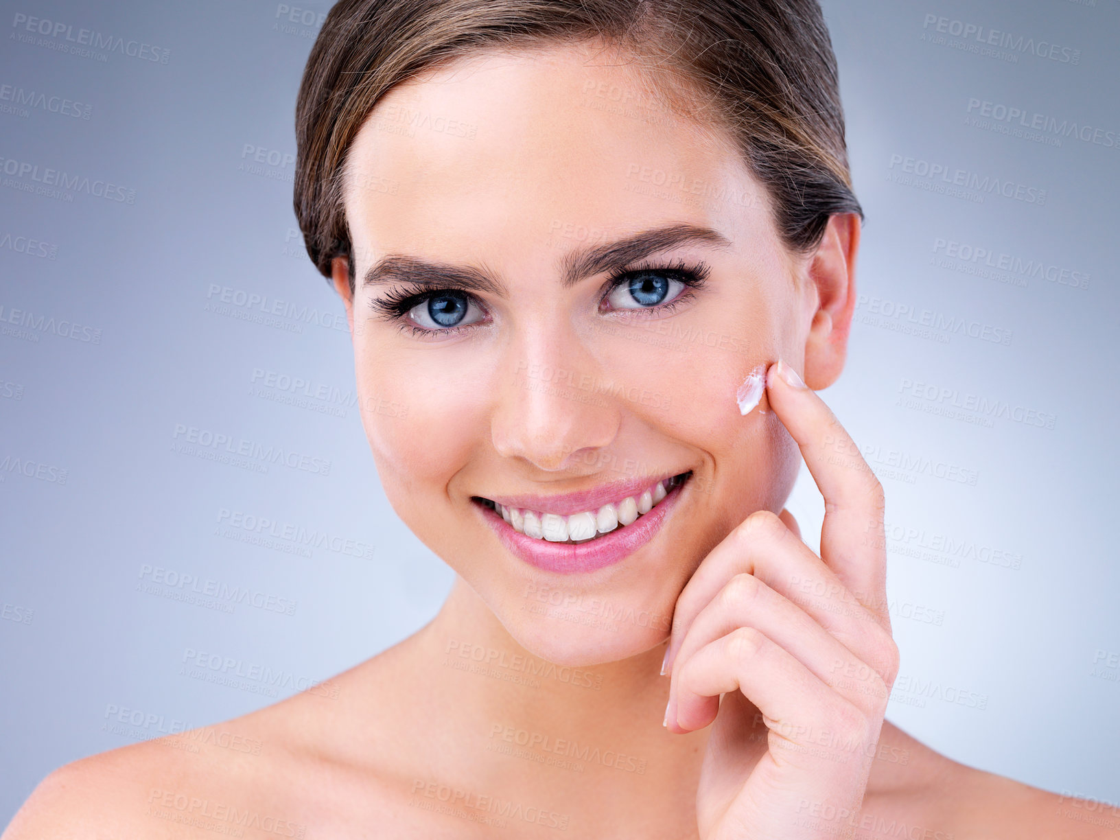 Buy stock photo Cropped shot of a young woman applying moisturizer to her face