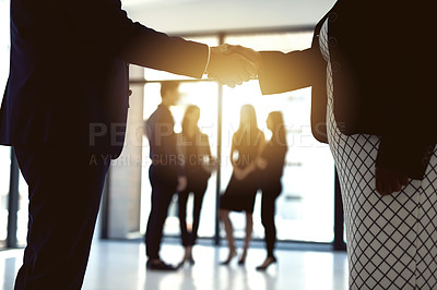 Buy stock photo Cropped shot of two businesspeople shaking hands in an office with colleagues in the background