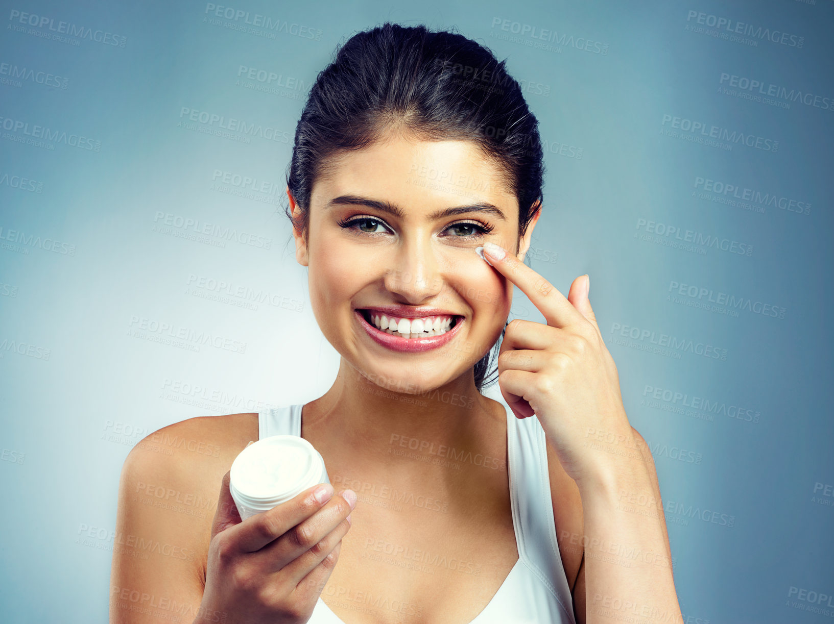 Buy stock photo Studio portrait of an attractive young woman applying moisturiser to her face