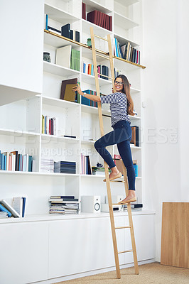 Buy stock photo Portrait of a smiling young woman climbing a ladder on a bookshelves at home