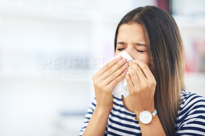 Buy stock photo Shot of a young woman with allergies sneezing into a tissue at home