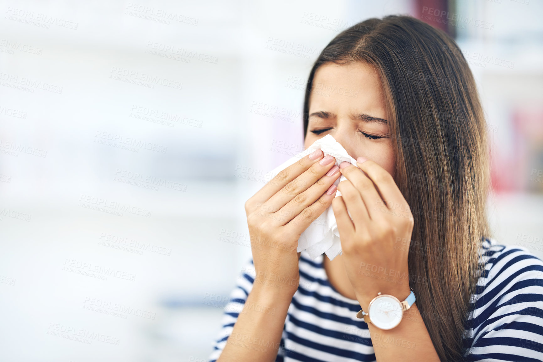 Buy stock photo Shot of a young woman with allergies sneezing into a tissue at home